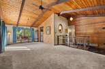 Experience rustic charm in this spacious living area featuring a vaulted wood-paneled ceiling with exposed beams and a ceiling fan.