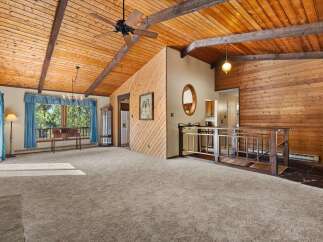 Experience rustic charm in this spacious living area featuring a vaulted wood-paneled ceiling with exposed beams and a ceiling fan.