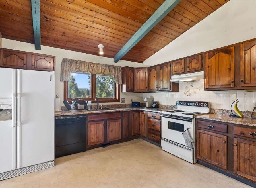 Discover a charming kitchen featuring warm wooden cabinetry and a vaulted wood-paneled ceiling with a decorative beam.