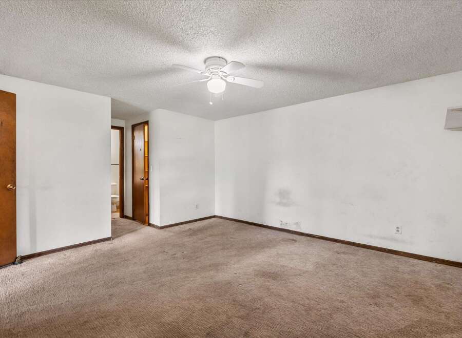 This spacious room features a neutral carpet and a white ceiling fan, perfect for creating a comfortable atmosphere.