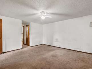 This spacious room features a neutral carpet and a white ceiling fan, perfect for creating a comfortable atmosphere.