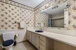 This charming bathroom features a floral wallpaper with a blue and yellow border, complemented by a white vanity with a navy sink and chrome fixtures.