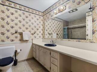 This charming bathroom features a floral wallpaper with a blue and yellow border, complemented by a white vanity with a navy sink and chrome fixtures.