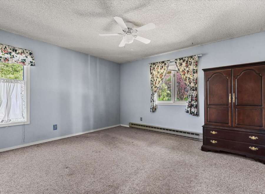 This spacious bedroom features a large window with floral curtains, allowing natural light to fill the room.