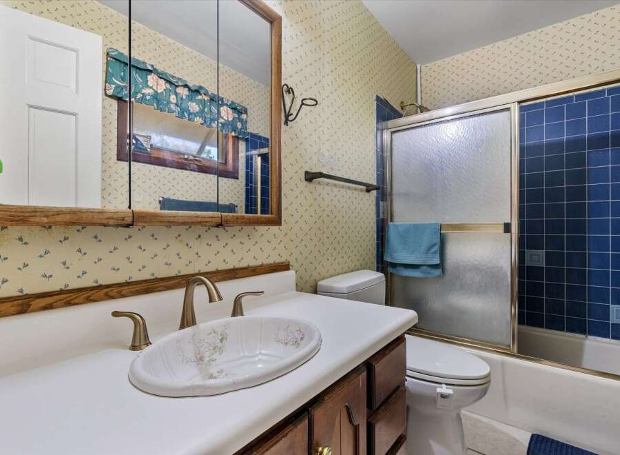 This bathroom features a charming floral wallpaper and a wooden vanity with a white countertop and sink.