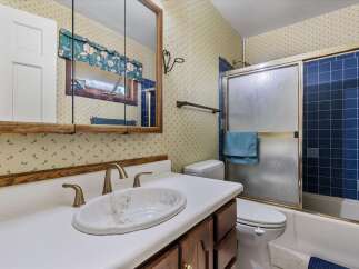 This bathroom features a charming floral wallpaper and a wooden vanity with a white countertop and sink.