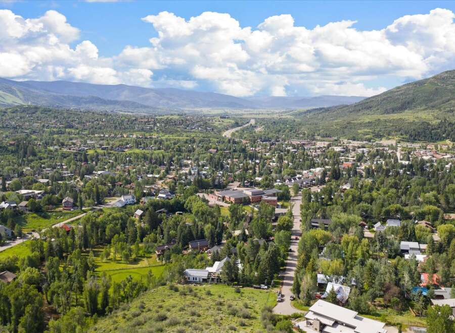 Discover this stunning aerial view of a picturesque mountain town nestled amidst lush green trees and rolling hills.