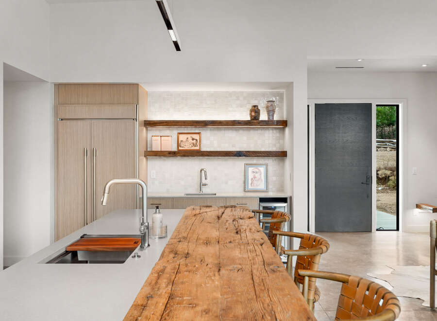Experience modern luxury in this stunning kitchen, featuring sleek cabinetry, a large island with a waterfall countertop, and a rustic wooden breakfast bar.