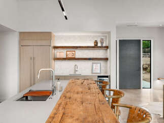 Experience modern luxury in this stunning kitchen, featuring sleek cabinetry, a large island with a waterfall countertop, and a rustic wooden breakfast bar.