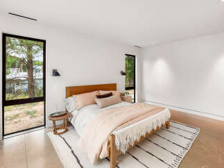 Experience modern comfort in this serene bedroom, featuring a plush bed adorned with soft, neutral-toned linens and accent pillows.
