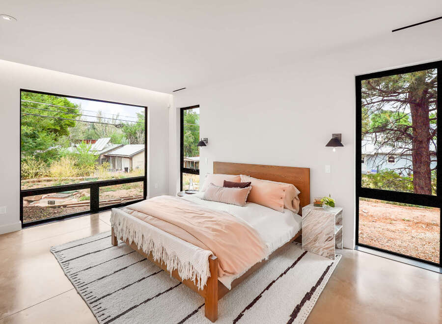 Experience modern living in this serene bedroom, featuring expansive windows that flood the space with natural light and offer picturesque views of the surrounding landscape.