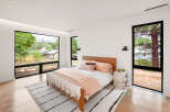 Experience modern living in this serene bedroom, featuring expansive windows that flood the space with natural light and offer picturesque views of the surrounding landscape.