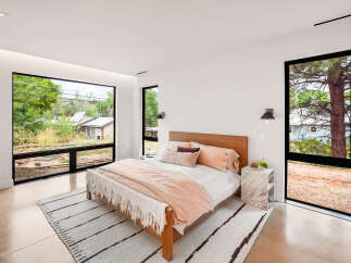 Experience modern living in this serene bedroom, featuring expansive windows that flood the space with natural light and offer picturesque views of the surrounding landscape.