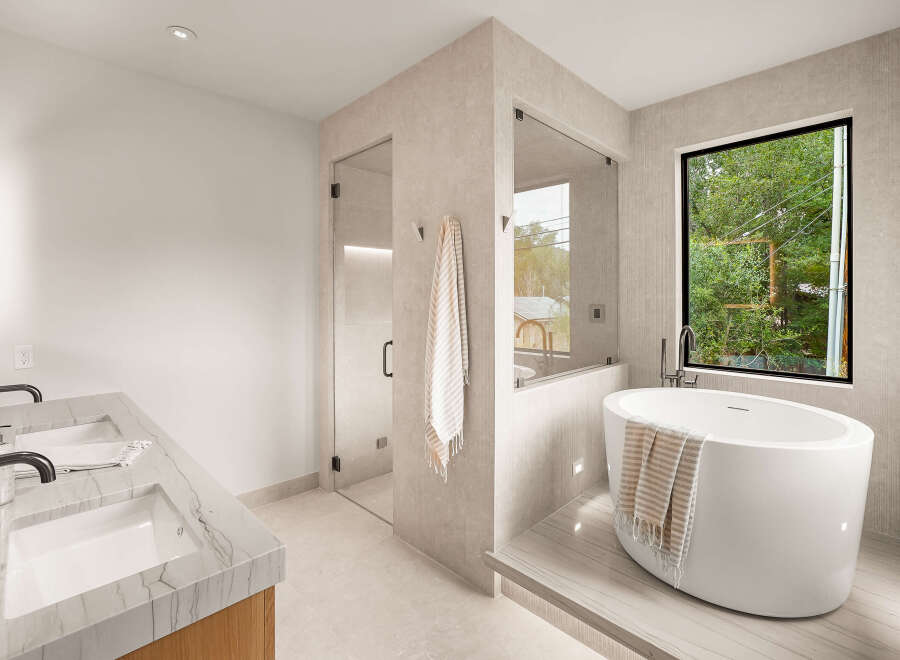 Experience modern luxury in this stunning bathroom, featuring a sleek freestanding bathtub positioned by a large window with lush green views.