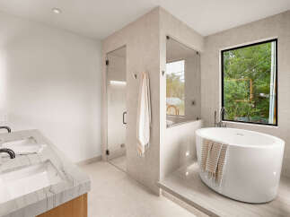 Experience modern luxury in this stunning bathroom, featuring a sleek freestanding bathtub positioned by a large window with lush green views.