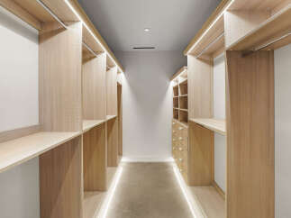 Step into this spacious walk-in closet, featuring custom light wood shelving and ample hanging space.