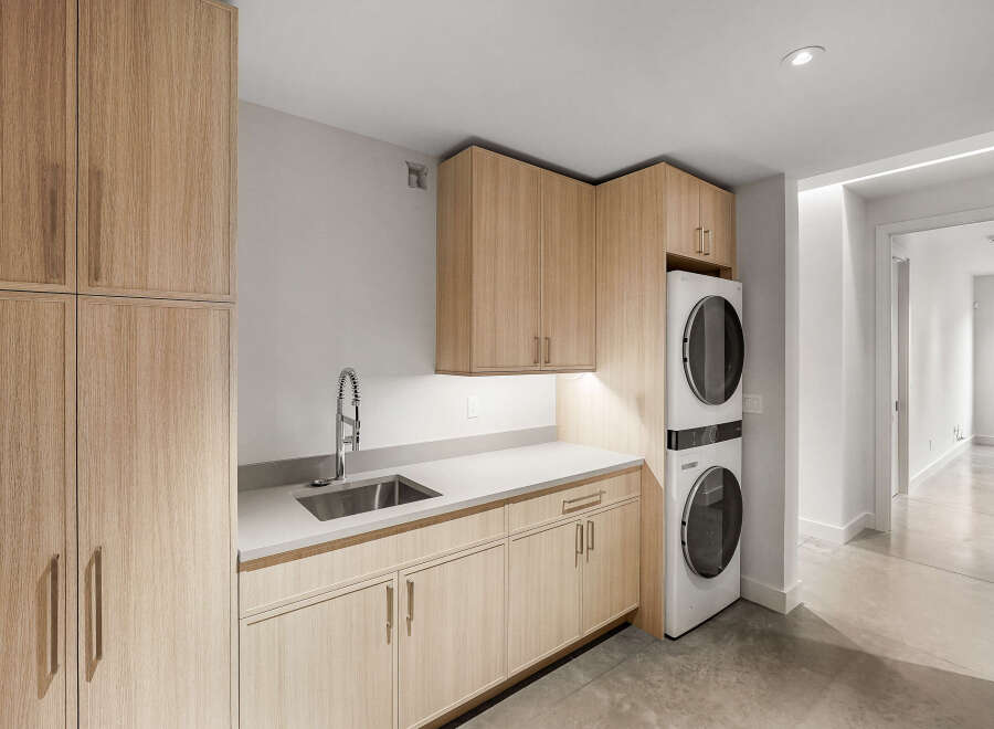 Discover this modern laundry room featuring sleek, light wood cabinetry and a durable quartz countertop.