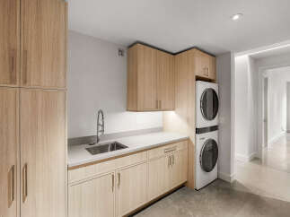 Discover this modern laundry room featuring sleek, light wood cabinetry and a durable quartz countertop.