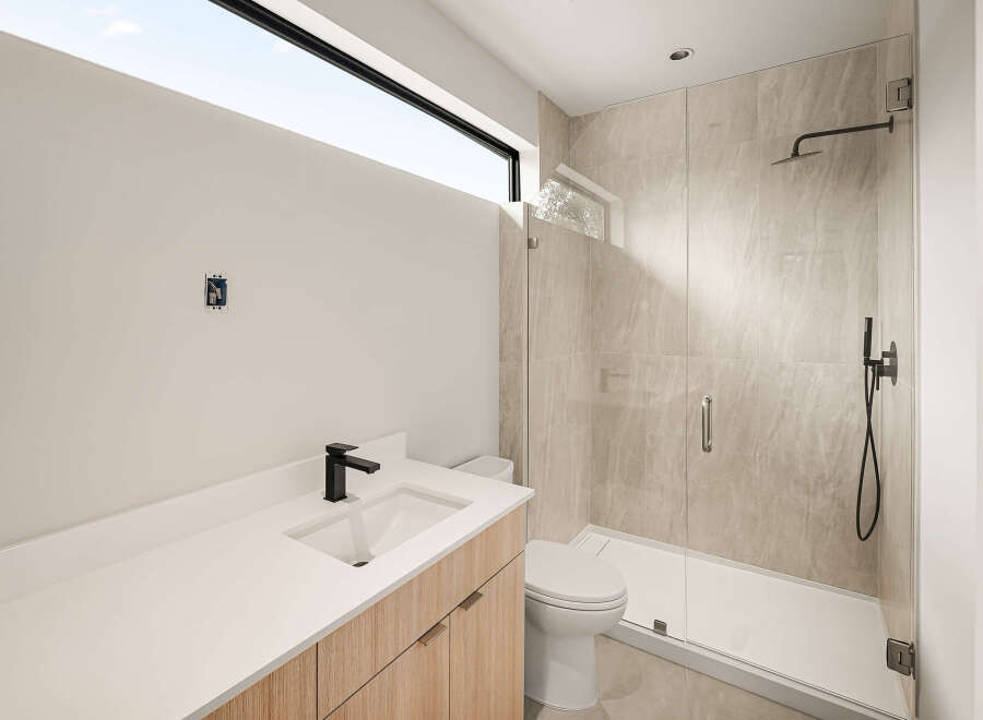 Experience modern luxury in this stunning bathroom featuring a sleek vanity with a black faucet and a spacious glass-enclosed shower with elegant tilework.