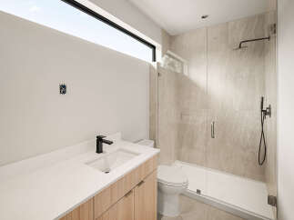 Experience modern luxury in this stunning bathroom featuring a sleek vanity with a black faucet and a spacious glass-enclosed shower with elegant tilework.
