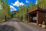 Discover this stunning property entrance featuring a secure black metal gate leading up a paved driveway, surrounded by a vibrant aspen forest.