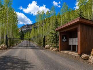Discover this stunning property entrance featuring a secure black metal gate leading up a paved driveway, surrounded by a vibrant aspen forest.