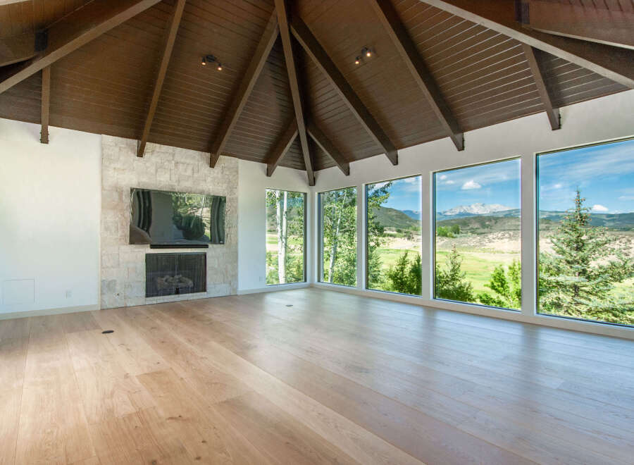 Experience breathtaking mountain views from this stunning living space, featuring a dramatic vaulted wood-beamed ceiling and a modern stone fireplace.