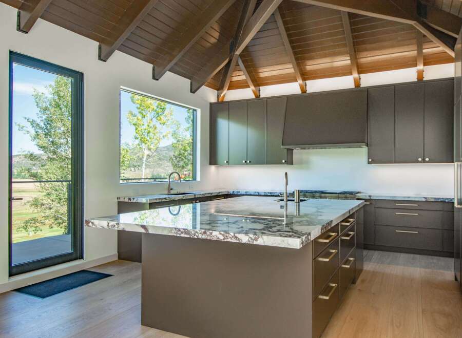 Experience modern luxury in this stunning kitchen, featuring sleek dark cabinetry and a dramatic vaulted wood ceiling.