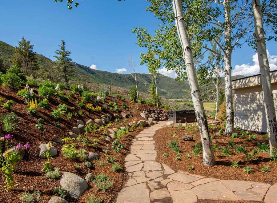 Discover this stunning mountain retreat featuring a beautifully landscaped hillside with vibrant flowers and natural stone pathways.