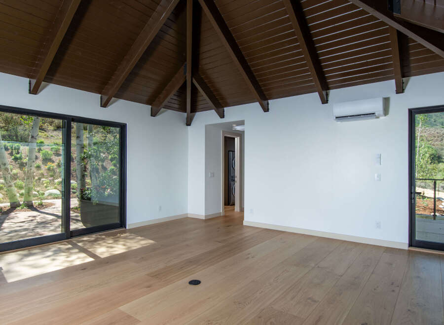 Experience modern living with this spacious room featuring a vaulted, dark wood beamed ceiling and large sliding glass doors that open to a scenic outdoor view.