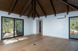 Experience modern living with this spacious room featuring a vaulted, dark wood beamed ceiling and large sliding glass doors that open to a scenic outdoor view.