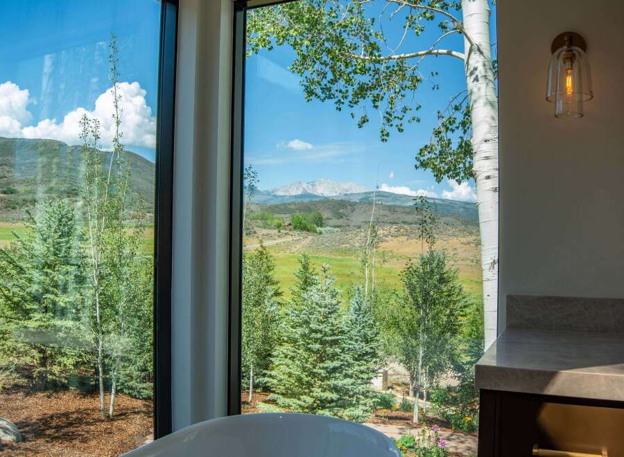 Experience breathtaking mountain views from this stunning property, framed by large windows and lush greenery.