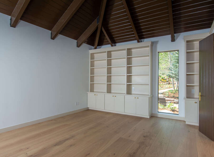 This room features a stunning vaulted ceiling with exposed dark wood beams, complemented by a built-in cream-colored bookshelf and cabinetry.