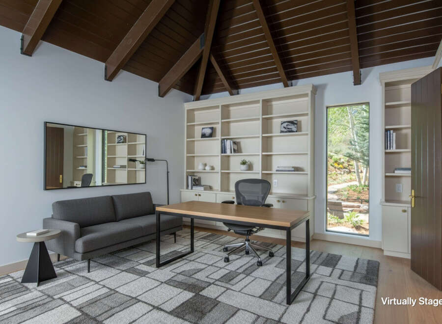 This beautifully staged home office features a spacious built-in bookshelf, a modern desk with an ergonomic chair, and a comfortable gray sofa.