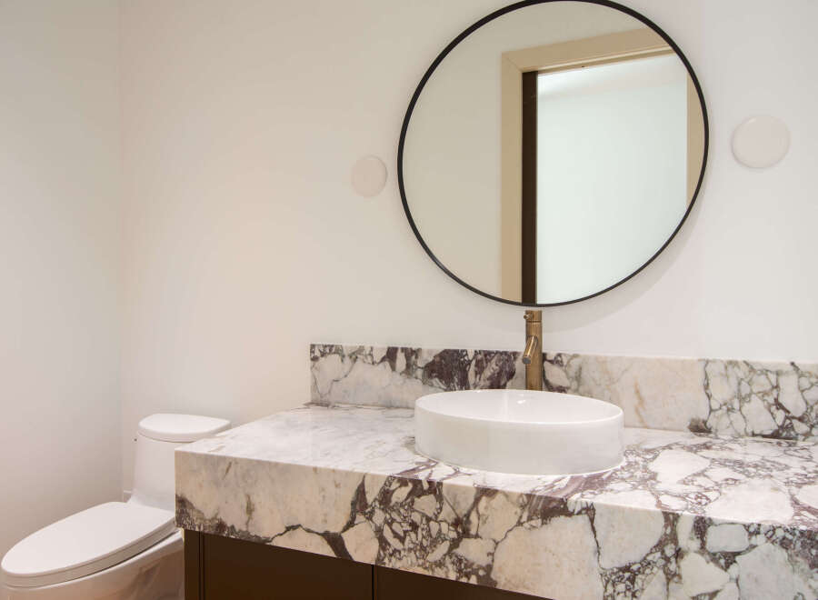 Experience modern luxury in this bathroom, featuring a striking marble vanity top that complements the sleek vessel sink and elegant brass faucet.