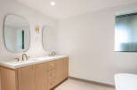 This modern bathroom features a double vanity with sleek gold fixtures and a light wood cabinet.