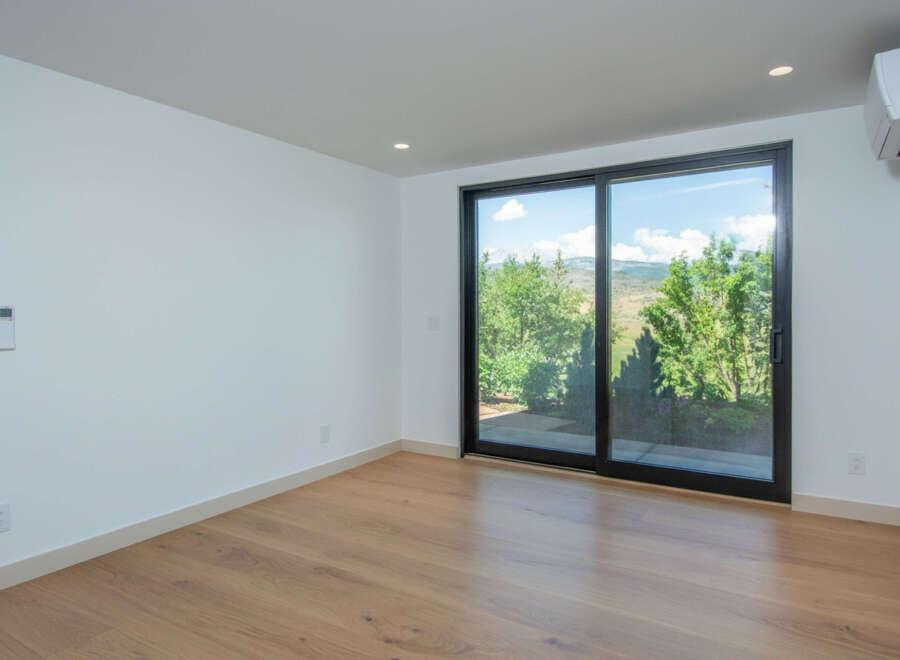 Experience modern living in this bright and airy room featuring a large sliding glass door that opens to a lush green landscape.