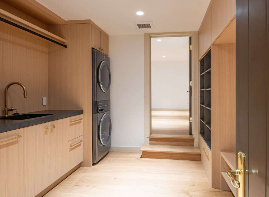 Discover modern convenience in this laundry room, featuring a stacked washer and dryer, a sleek sink with a gooseneck faucet, and ample storage.