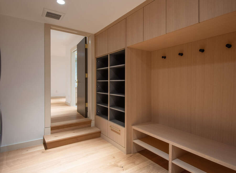 This modern laundry room and mudroom features a stacked washer and dryer unit, a built-in bench with shelving, and ample storage cabinets.