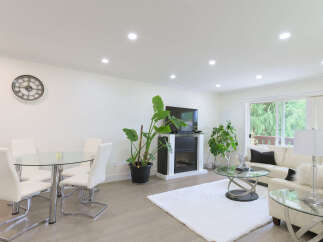 This spacious living and dining area features a modern glass-top dining table with white chairs, perfect for family meals.