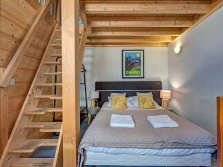 Experience cozy mountain living in this charming bedroom featuring a comfortable bed adorned with plush pillows and crisp white towels.