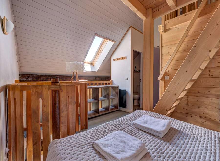 Experience cozy living in this charming loft bedroom, featuring a comfortable bed adorned with fresh white towels.