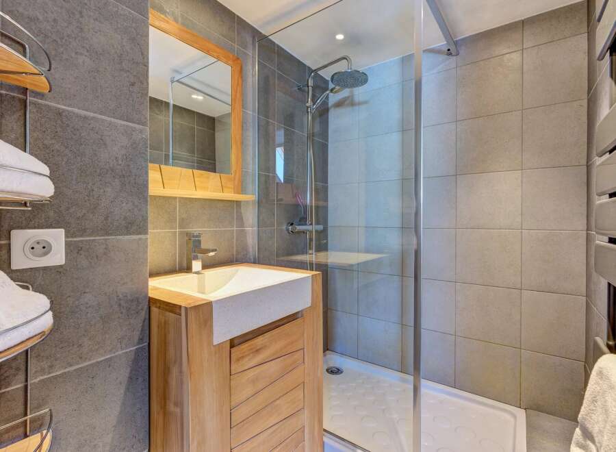 This modern bathroom features a sleek vanity with a stone countertop and a wooden cabinet, complemented by a spacious walk-in shower with a rainfall showerhead.