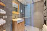 This modern bathroom features a sleek vanity with a stone countertop and a wooden cabinet, complemented by a spacious walk-in shower with a rainfall showerhead.