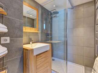 This modern bathroom features a sleek vanity with a stone countertop and a wooden cabinet, complemented by a spacious walk-in shower with a rainfall showerhead.