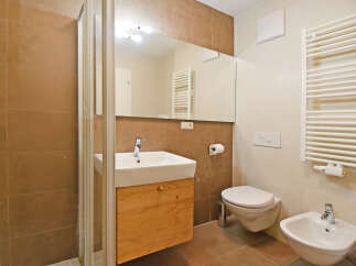 This modern bathroom features a sleek white sink with a wooden vanity, a glass-enclosed shower, and a wall-mounted toilet and bidet.