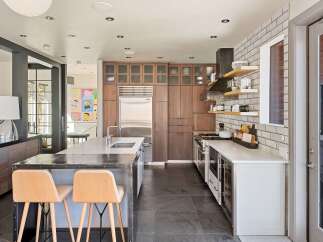 This modern kitchen boasts a sleek stainless steel island with a double sink and two stylish wooden bar stools, perfect for casual dining.
