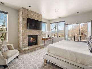 Experience luxury mountain living in this stunning bedroom featuring a modern stone fireplace and a wall-mounted TV.
