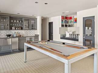 Experience ultimate entertainment in this stylish game room, featuring a sleek pool table and a well-appointed bar area with ample glassware and a wine fridge.