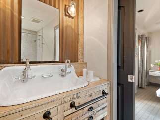 This bathroom features a rustic charm with its corrugated metal accent wall and a vintage-inspired double basin sink set atop a distressed wood vanity.